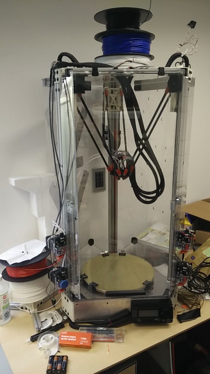 The finished delta printer in its clear enclosure, with filament spools on top and a round bed at the bottom