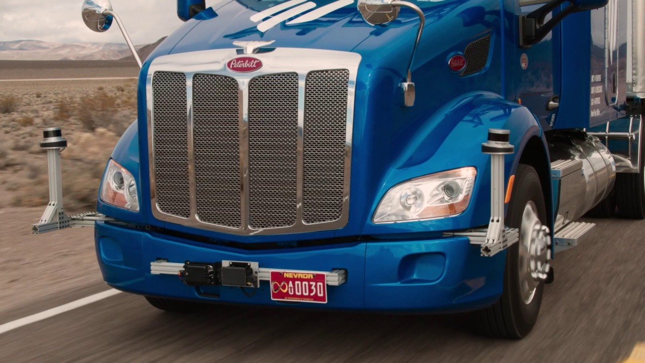 Front of Embark's blue Peterbilt prototype on a desert highway, with sensors on mounts at both front corners and on the bumper