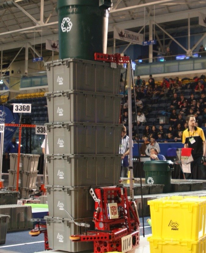 Team 1114’s robot holding a stack of six grey boxes with a green bin on top
