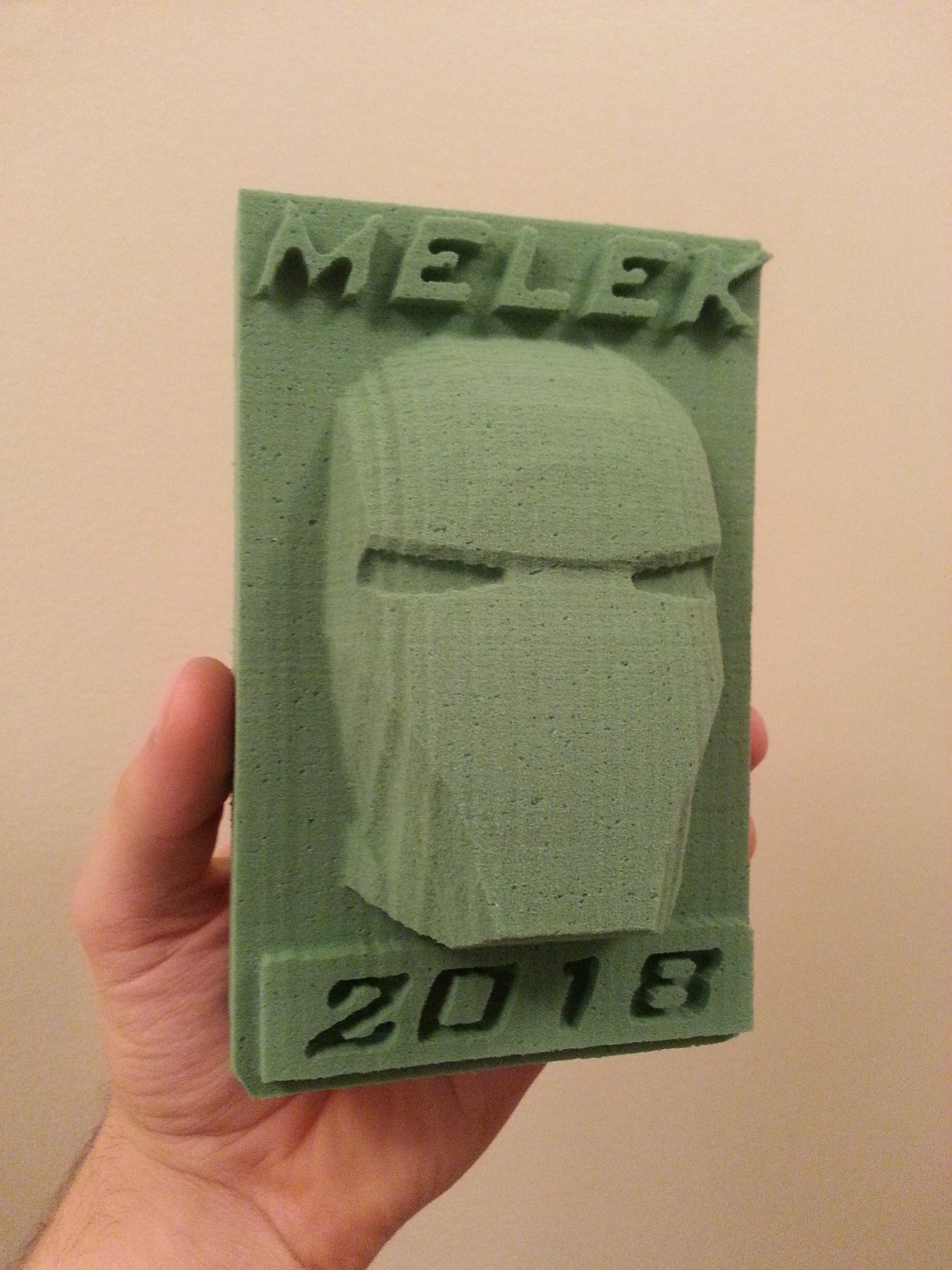 An Iron Man helmet carved in relief from green floral foam, with lettering above and below, held in a hand