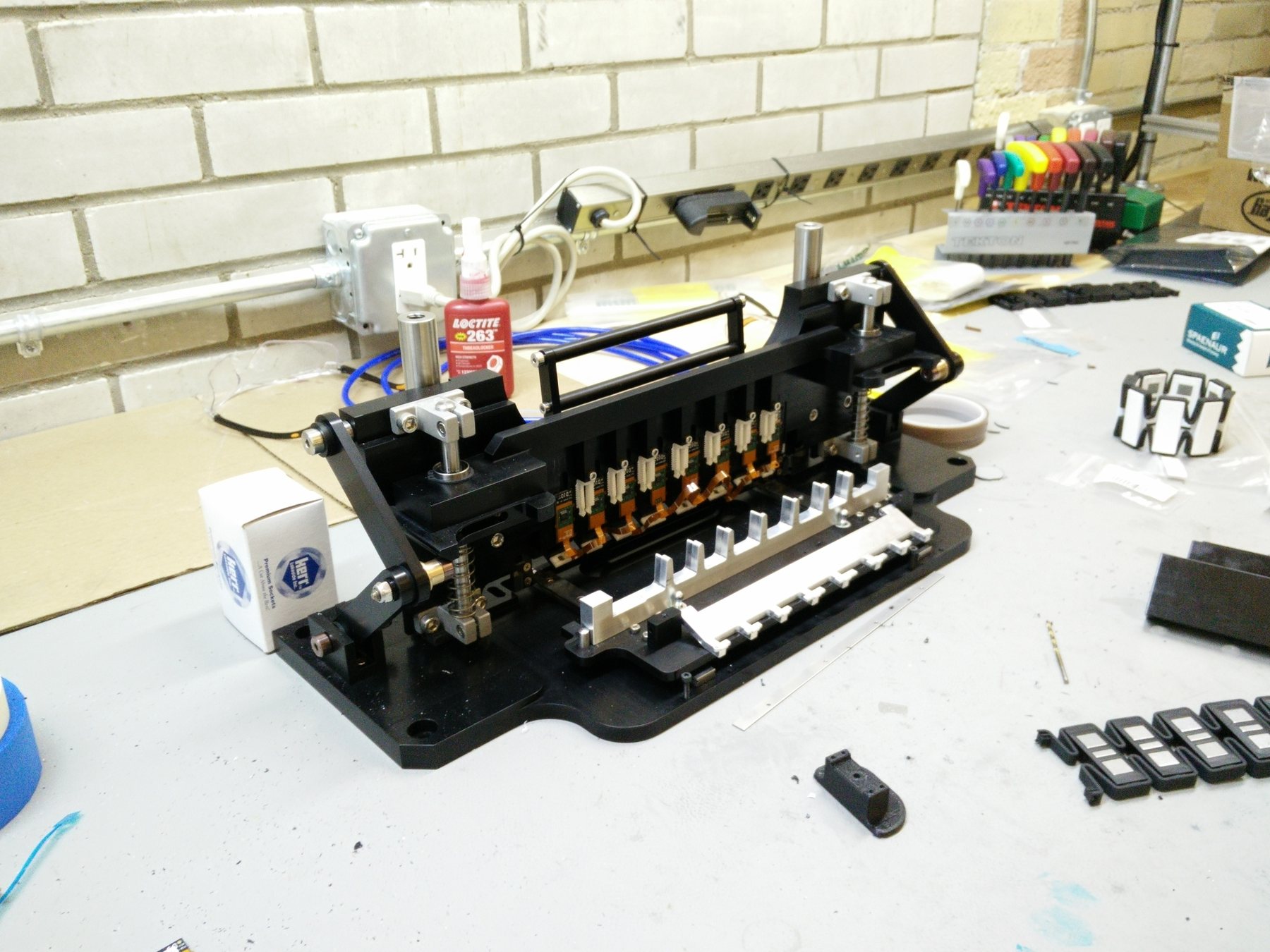 The finished jig on a workbench, with the orange flexible PCB zig-zagging across its pod stations