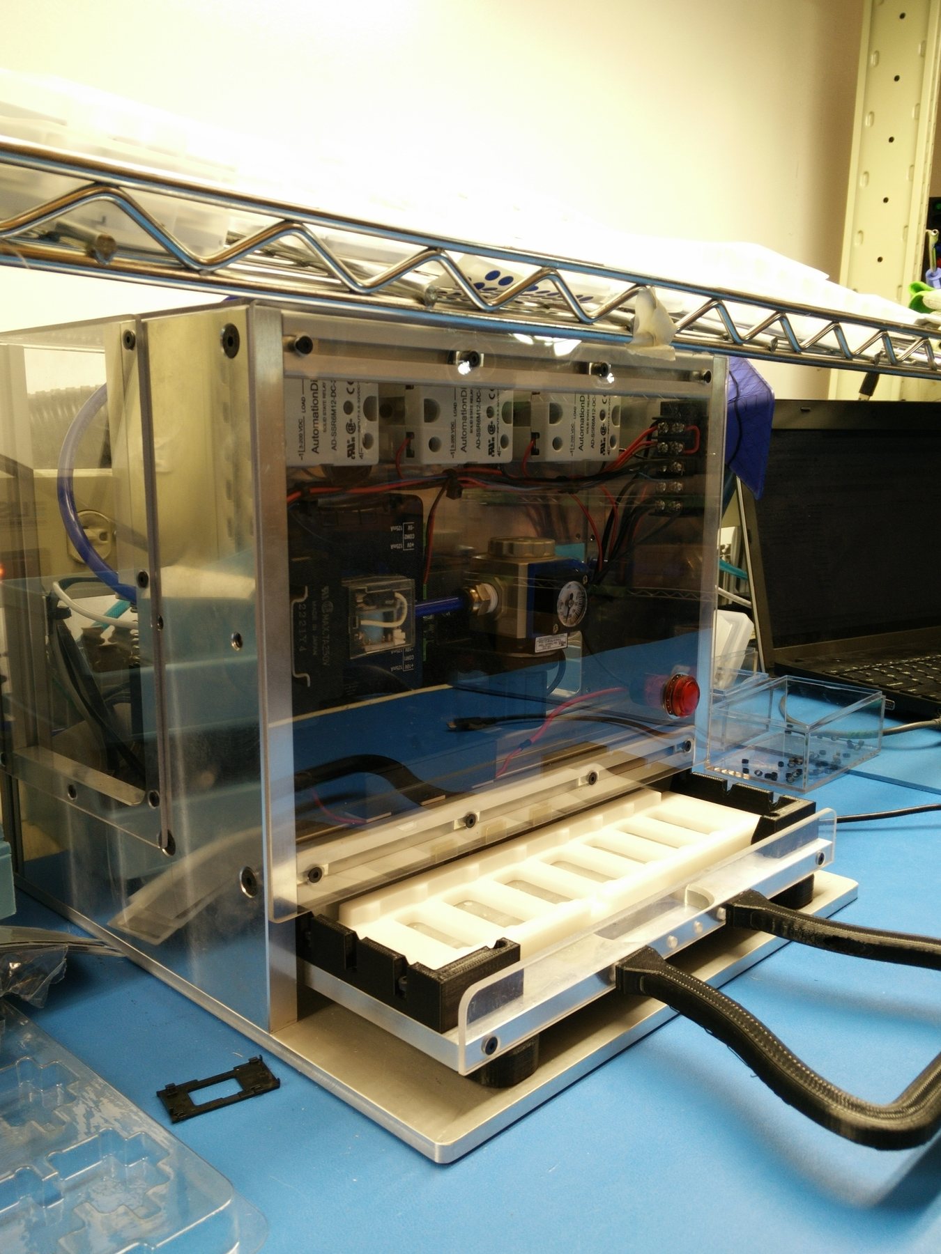 The benchtop pneumatic pod press behind clear guards, with its relays and air regulator visible above the loading tray