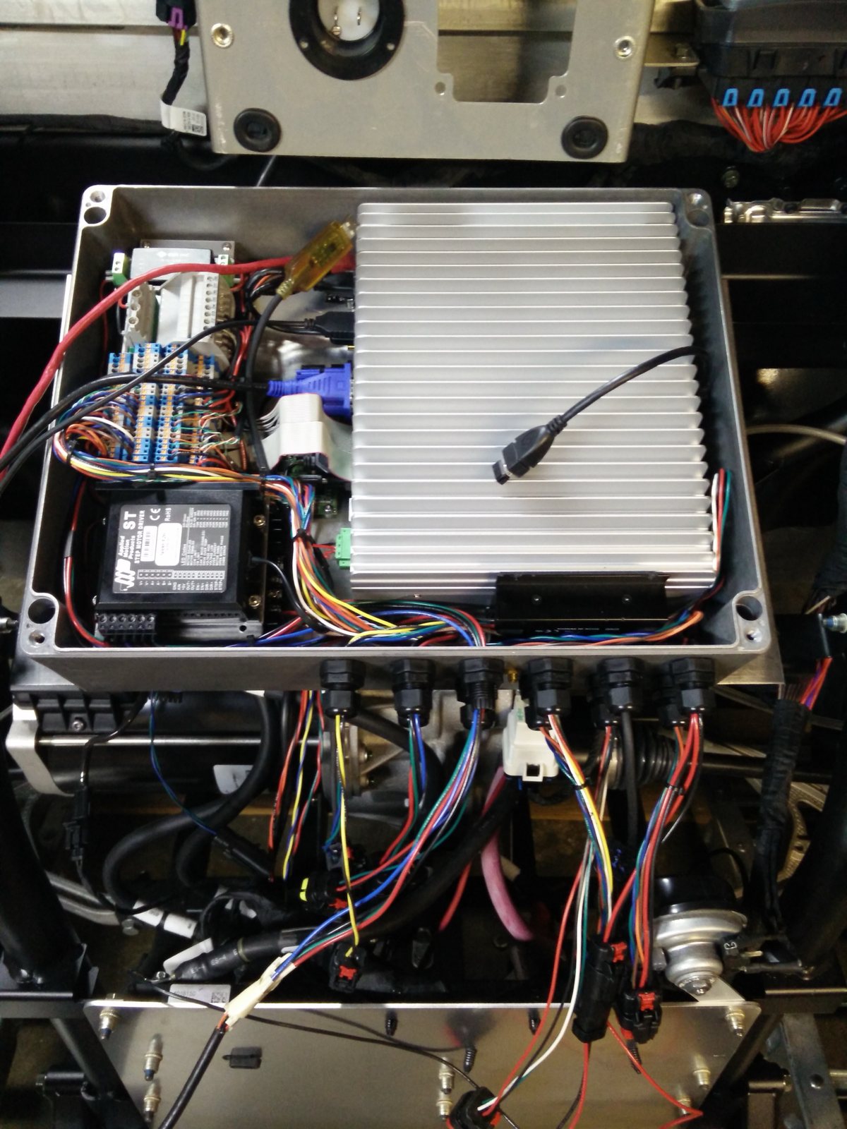 Open MVP enclosure in the vehicle: a finned ruggedized computer, a stepper motor driver, terminal blocks and a row of cable glands