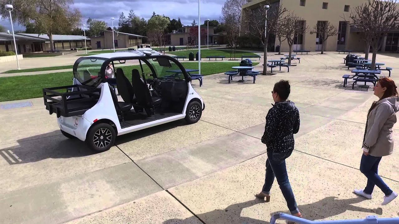 Gen 2 shuttle in a campus courtyard, with two people walking towards it